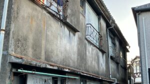 築年数が経過し、外壁の劣化や錆びた鉄製手すりが目立つアパートの外観。老朽化によるリフォームの必要性が見て取れる。